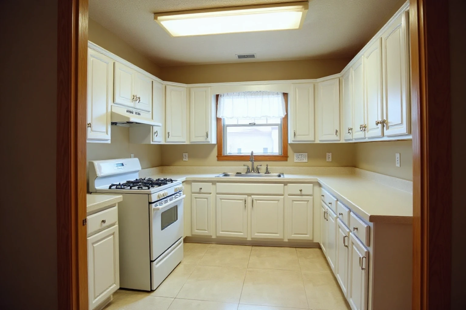 U-shaped kitchen refaced with painted white doors and drawer fronts, almond laminate counters, white gas range and fluorescent light.